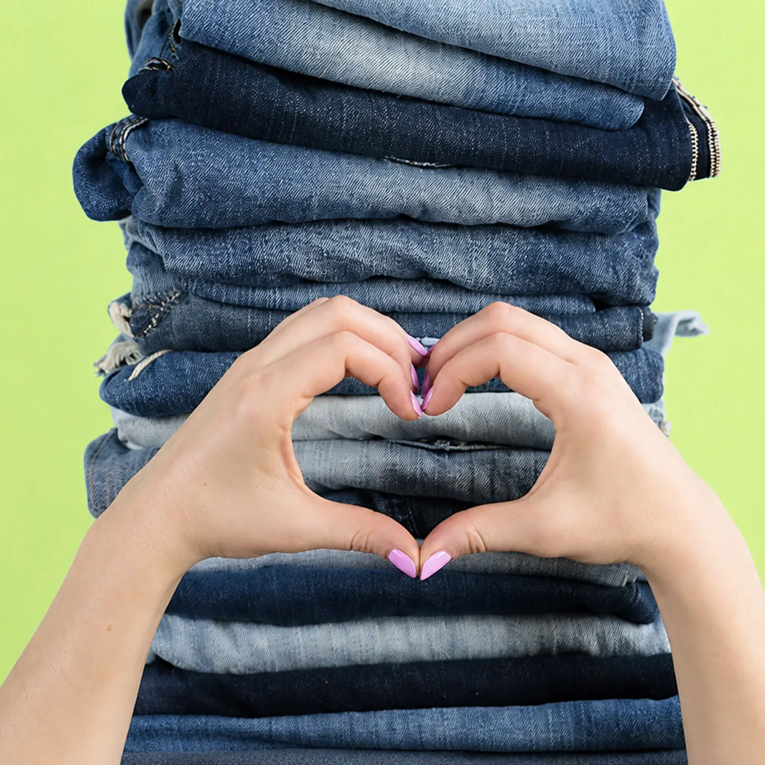 Mains formant un cœur devant une pile de vieux jeans, une image qui évoque notre relation aux vêtements et à la mode.